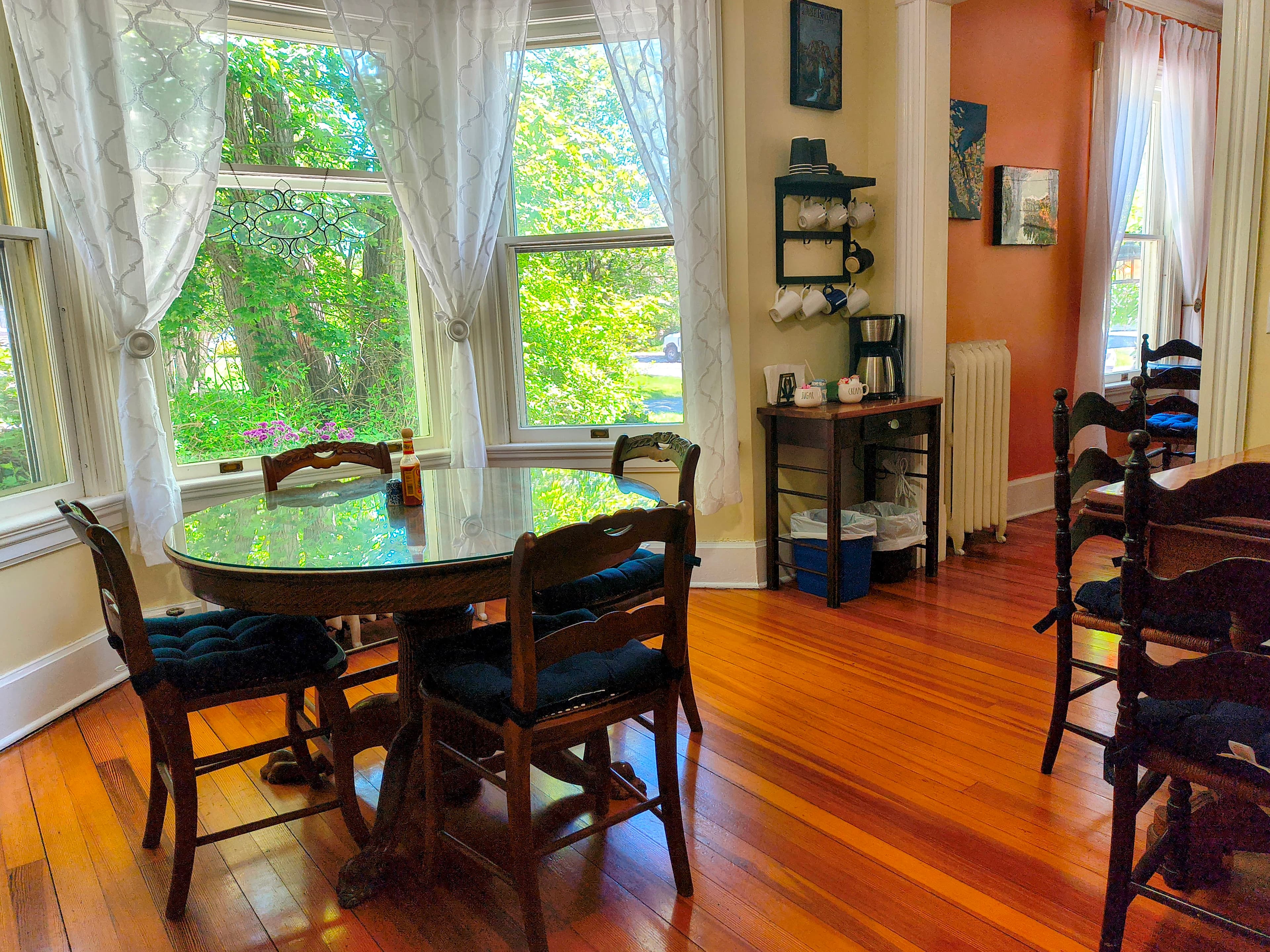 A cozy dining area with a round table, wooden chairs, large windows, and warm wooden floors.