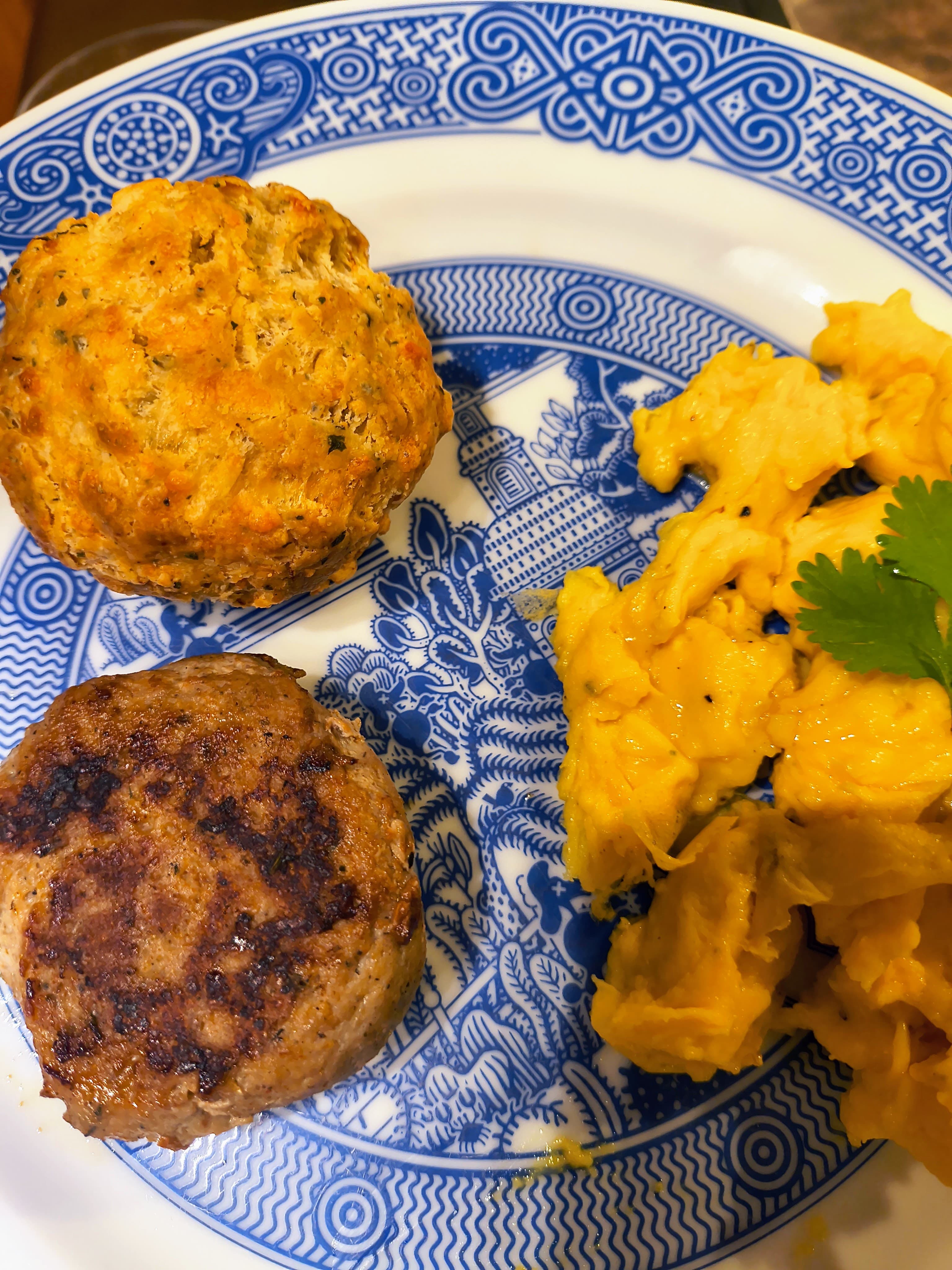 A plate featuring two golden biscuits and scrambled eggs with a sprig of cilantro.