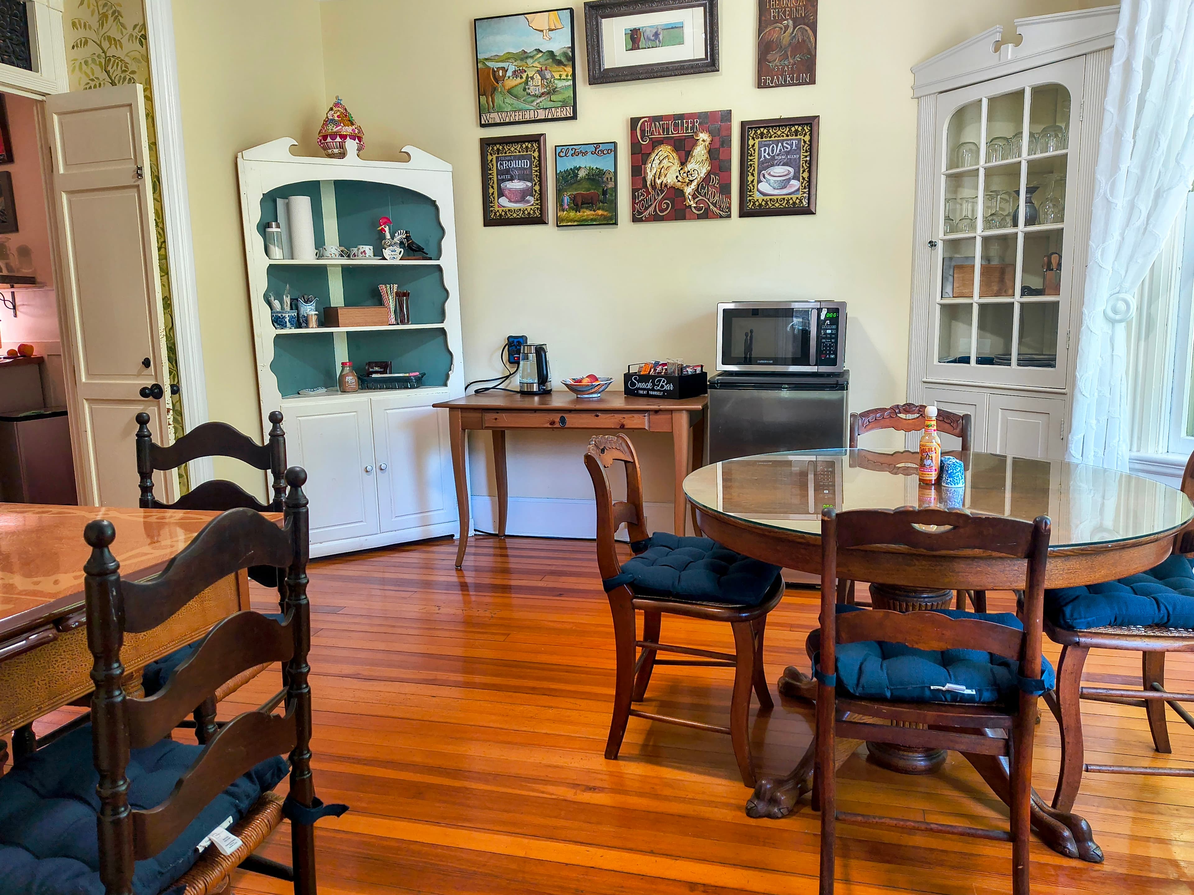 A cozy dining area featuring a round table, wooden chairs, and a vintage cabinet, with framed artwork on the walls.
